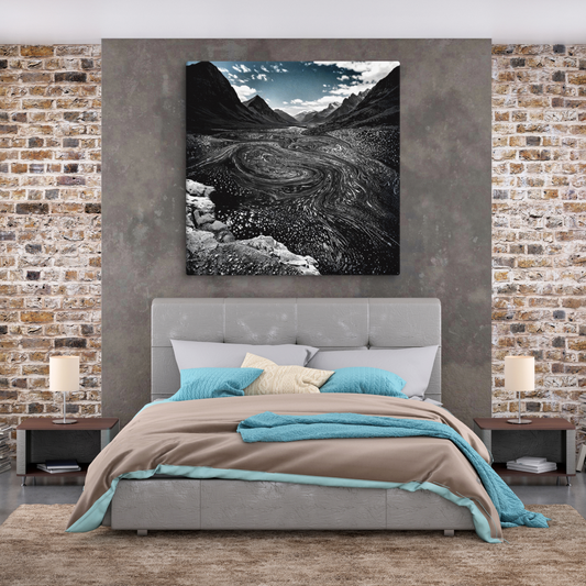 Black-and-white aerial view of a dramatic glacial river carving through rugged mountain valleys.